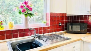 Eine Küche mit Spüle, Geschirrgestell, Mikrowelle und einem Fenster mit Blumenarrangements.