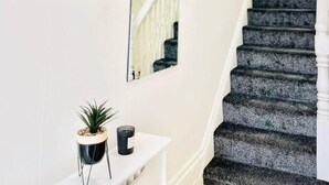 Eine Treppe mit dunklem Teppich, einer weißen Wand und einer hängenden Pflanze.