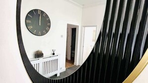 A room with a round mirror reflecting a clock and a white console table with decorative items. - Portsmouth Apartment - Seaside Gem (Portsmouth)