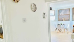 Een modern interieur met een witte muur, een plafondlamp en een eethoek met een tafel en stoelen.