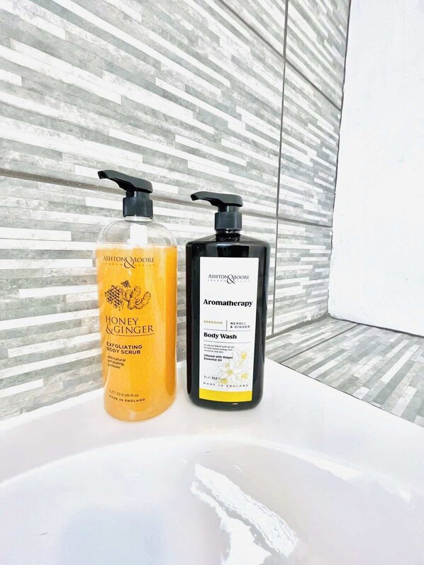 Deux bouteilles de gel douche Ashton's Moore sur un lavabo blanc, avec un mur texturé en arrière-plan.