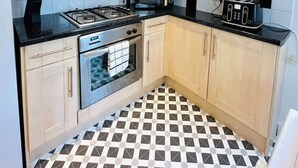 A compact kitchen with light wooden cabinets, a gas stove, a microwave, a toaster, and a patterned floor. - Clarence Road: Cozy King Room in Portsmouth (Portsmouth)
