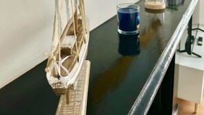 A room with a black countertop, a decorative sailboat, a mirror with a wavy gold frame, a blue glass, and a small plant in a glass container. - Portsmouth Apartment: Cozy & Convenient Location (Portsmouth)