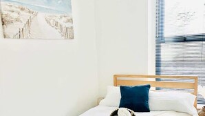 A bedroom with a wooden bed, white bedding, a blue pillow, a blue throw blanket, and a small rug. - Portsmouth Apartment: Cozy & Convenient Location (Portsmouth)