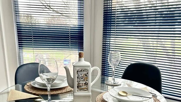 A dining area with a glass table set for four, surrounded by chairs. - Portsmouth Apartment: Cozy & Convenient Location (Portsmouth)