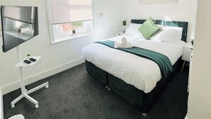Une chambre moderne comprenant un lit, un bureau, une chaise, un téléviseur et une fenêtre avec des stores.