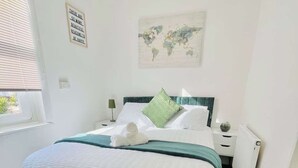 Un lit bien fait, avec une couette verte et blanche, une carte du monde accrochée au mur et une citation inspirante.