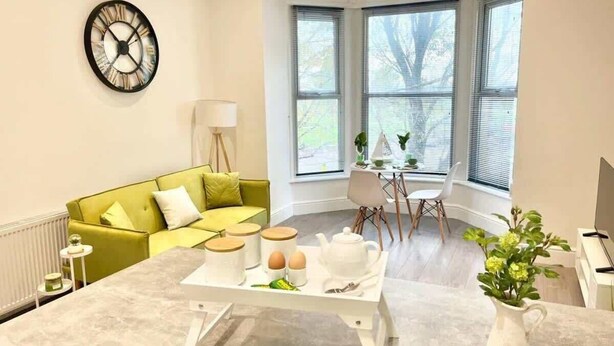 Eine moderne Küche mit Marmorarbeitsplatte, einem grünen Sofa, einem Esstisch mit Stühlen und großen Fenstern mit Jalousien.