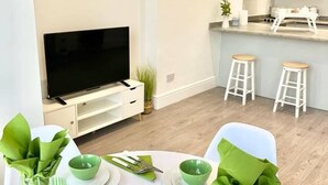 Ein modernes Wohnzimmer mit Essbereich, Fernseher und einer Küche im Hintergrund.