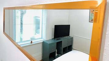 A bedroom with a bed, a dresser, a television, and a window with blinds.