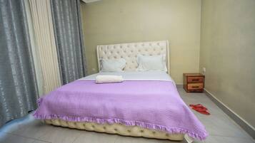 A neatly made bed with a purple bedspread, a white pillow, and a wooden nightstand with a drawer.