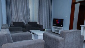 A living room with grey sofas, a white coffee table, and a flat-screen TV on a stand. - VYREX RESIDENCE (Kigali)