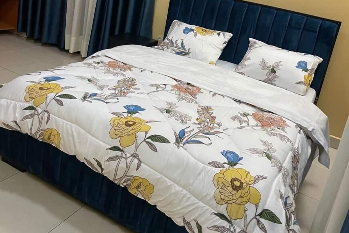 Una cama con edredón floral, cabecera azul oscuro y almohada blanca con estampado floral azul.