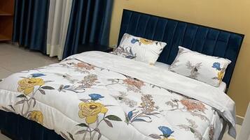 En säng med ett blommigt överkast, en mörkblå sänggavel och en vit kudde med ett blått, blommigt mönster.
