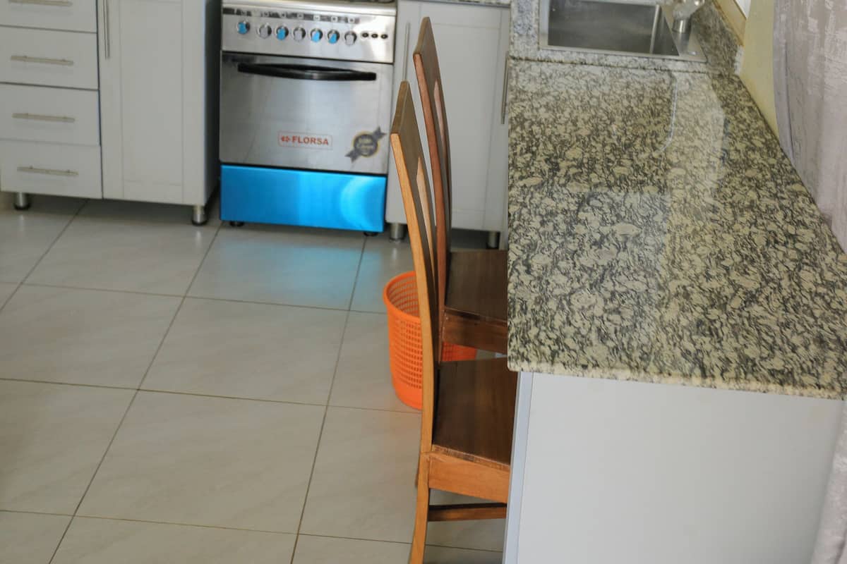 Una cocina con armarios blancos, estufa, microondas, lavaplatos y una silla.