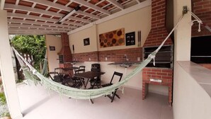 A covered outdoor area with a brick fireplace, a dining table with chairs, and a hammock.
