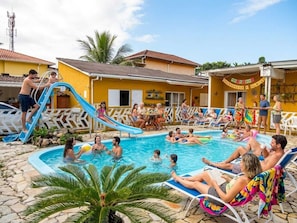 Un espace piscine avec un toboggan, des chaises longues et un bùtiment à la façade jaune.