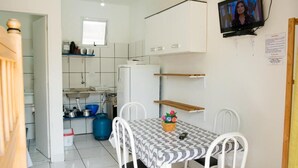 A compact kitchen with white cabinets, a blue gas cylinder, and a dining area with a patterned tablecloth and white chairs.