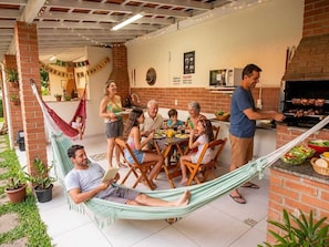 Une famille prend son repas Ă lâextĂ©rieur, sur une terrasse en briques, prĂšs dâun hamac et dâun espace barbecue.