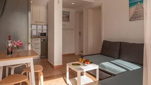 A modern living room with a sofa, a dining table with chairs, a small kitchen area, and a breakfast tray on the table. - Casita Lola - Sunny Apartment in the closed complex with a swimming pool. (Costa Calma)