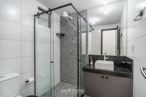 Ein modernes Badezimmer mit einer Duschkabine aus Glas, einer schwarzen Ablagefläche und einem weißen Waschbecken.
