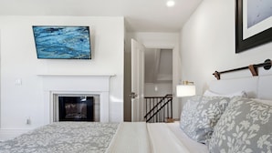 A bedroom with a bed, a fireplace, a painting, and a staircase. - Boothbay Harbor King Suite - Room 4 at Greenleaf Inn - Fireplace, Harbor Views! (Boothbay Harbor)
