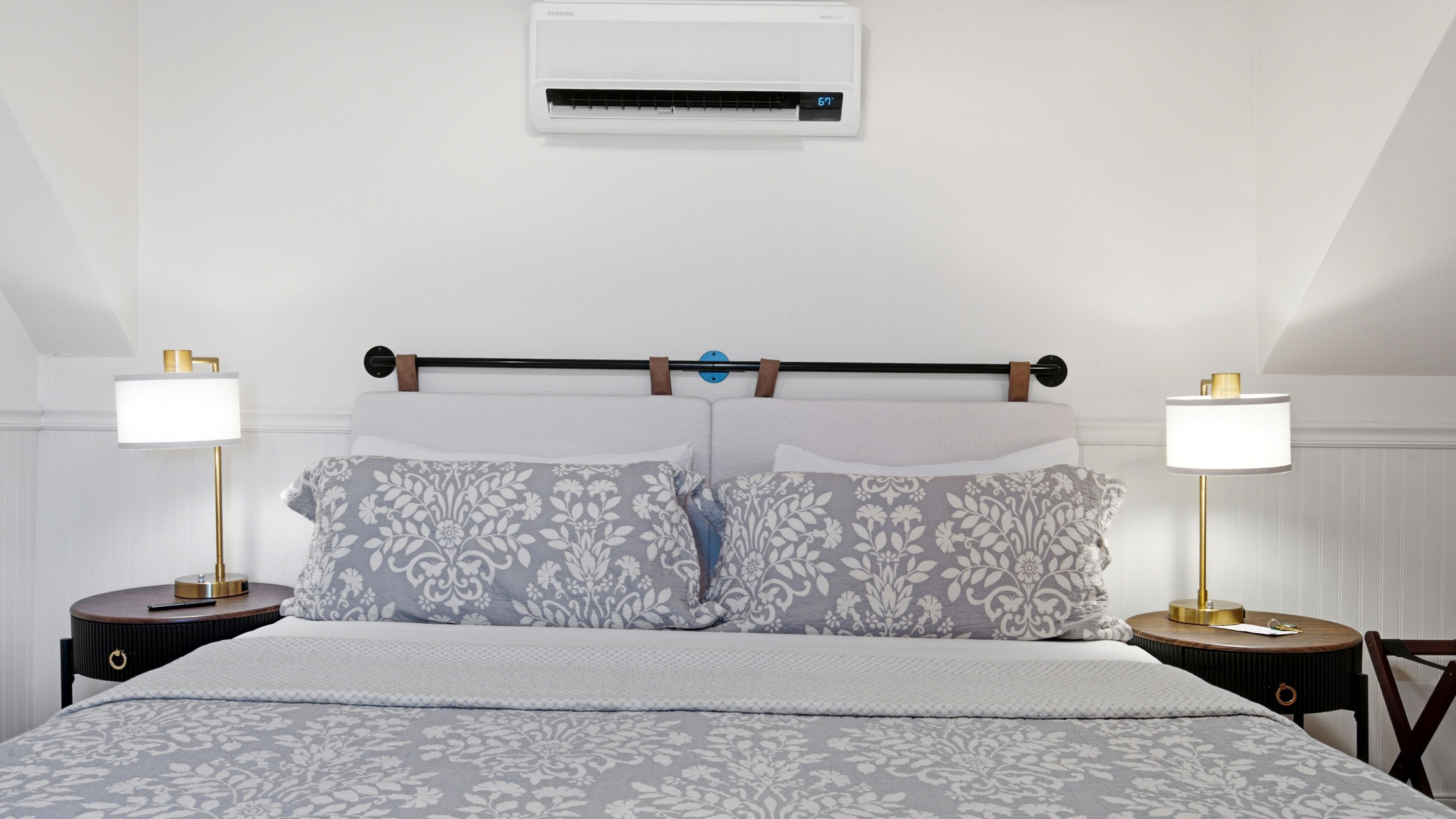 A neatly made bed with patterned bedding, a wall-mounted air conditioner, and two bedside lamps on either side.