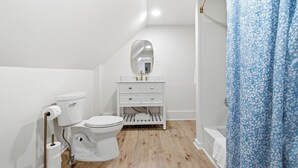 Ein kleines, weißes Badezimmer mit Toilette, Waschbecken, Spiegel und Duschvorhang.