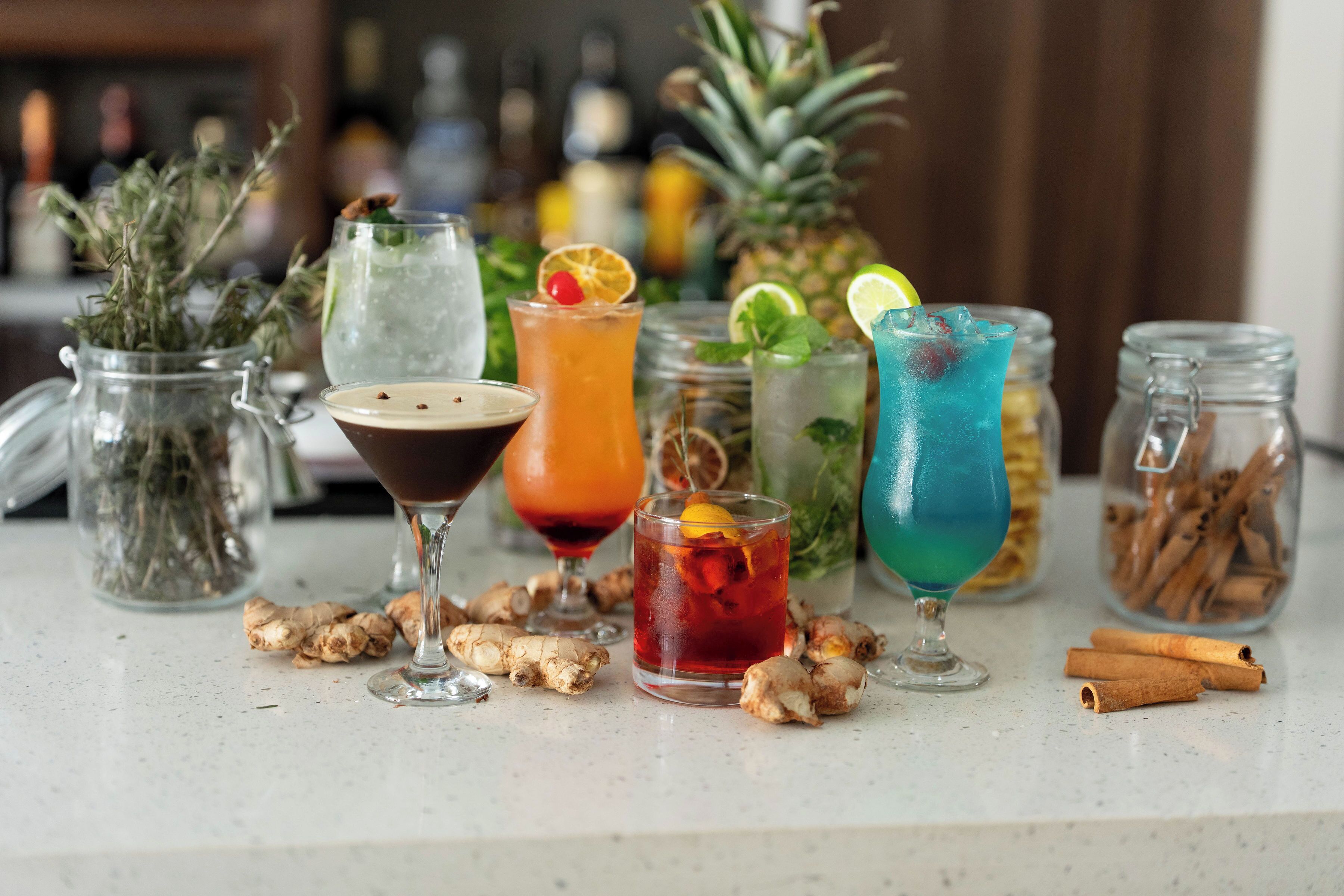 Une variété de boissons est présentée sur le comptoir d’un bar, avec des tranches de gingembre et des bâtons de cannelle.
