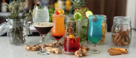 Une variété de boissons est présentée sur le comptoir d’un bar, avec des tranches de gingembre et des bâtons de cannelle.
