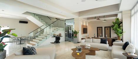 A spacious living area with a staircase, a dining area, and a seating area with sofas and coffee tables.