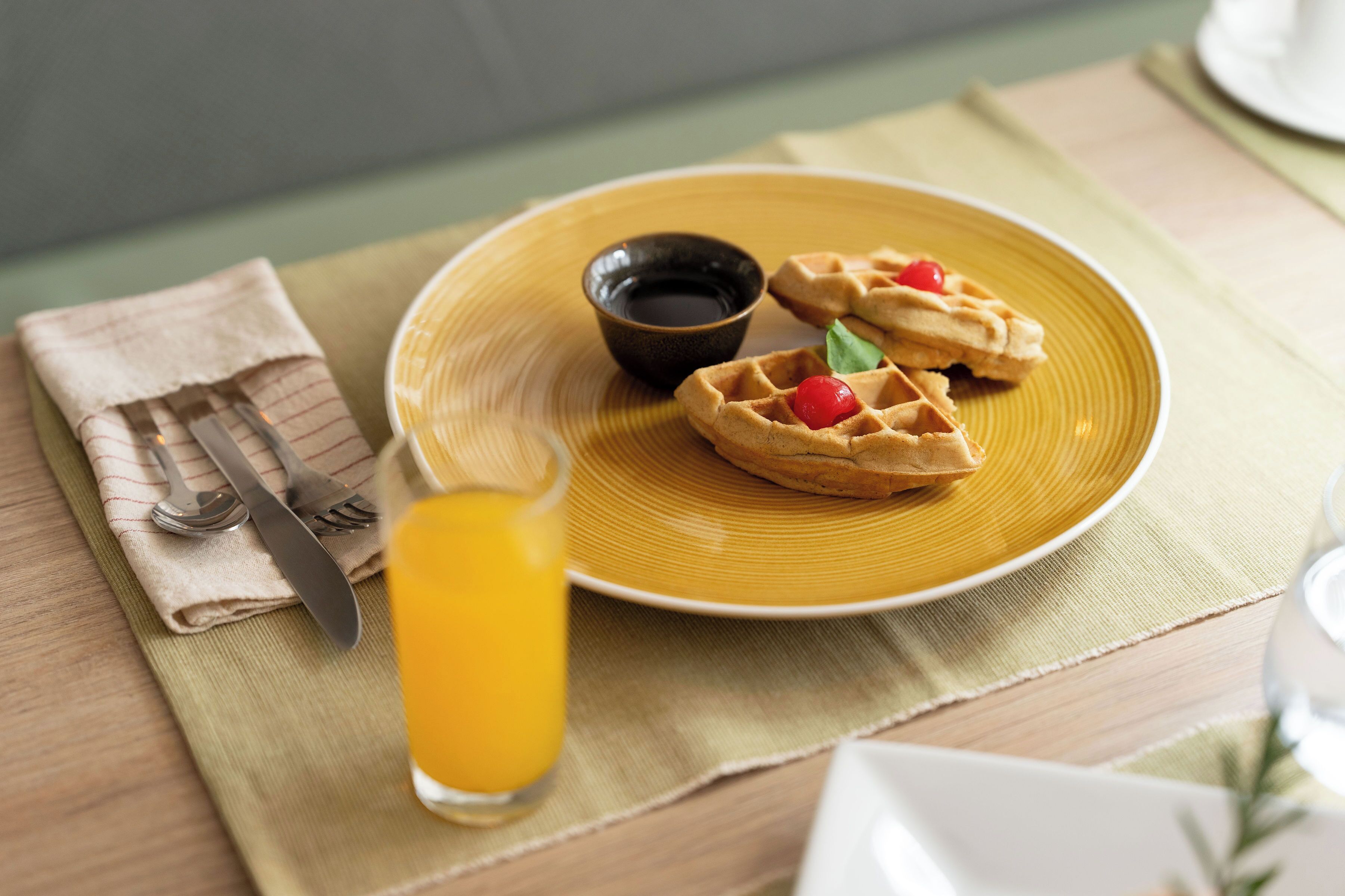 A breakfast setting with waffles, syrup, and a glass of orange juice on a yellow plate.