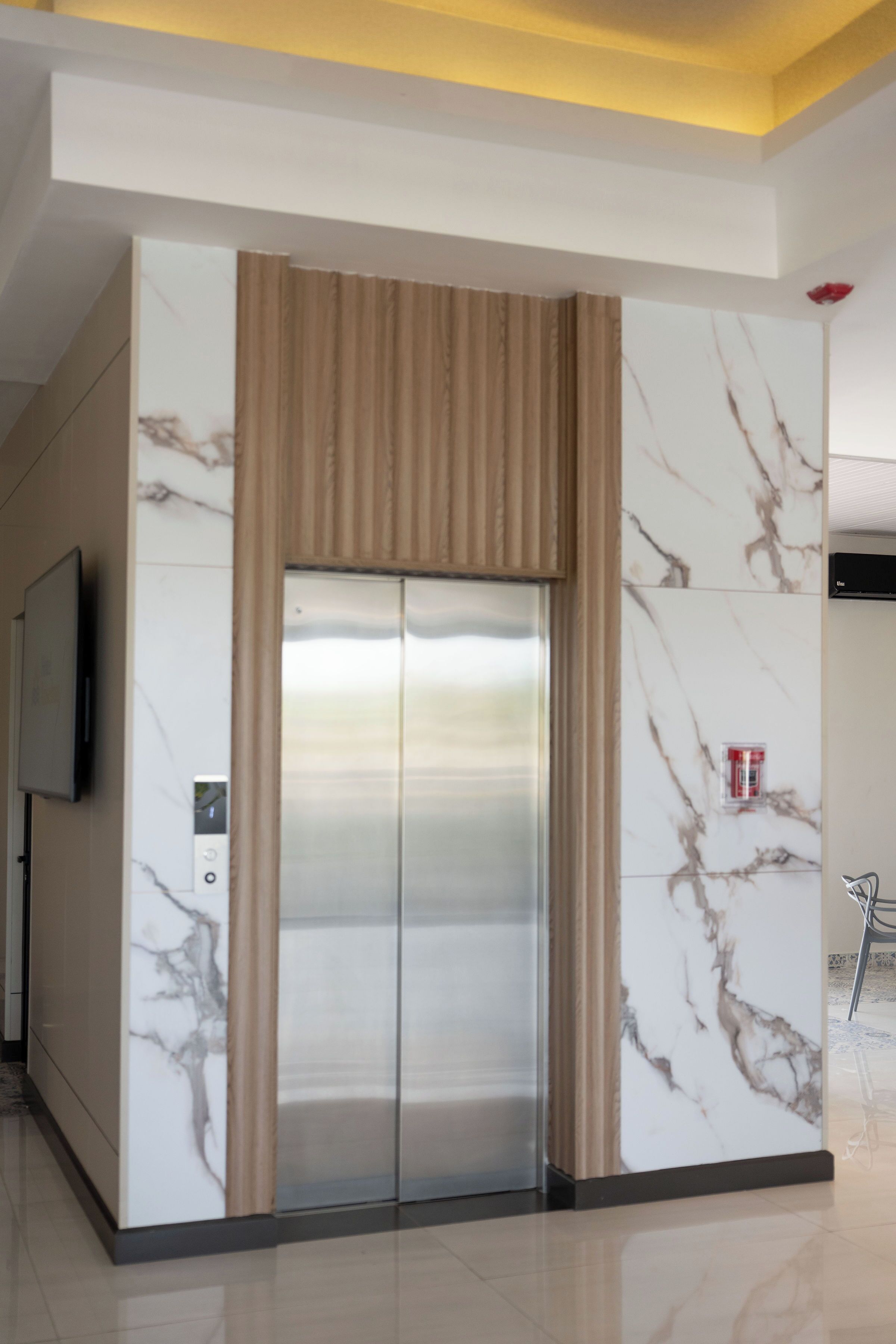 An elevator with a marble wall design, a modern control panel, and a television mounted on the wall.