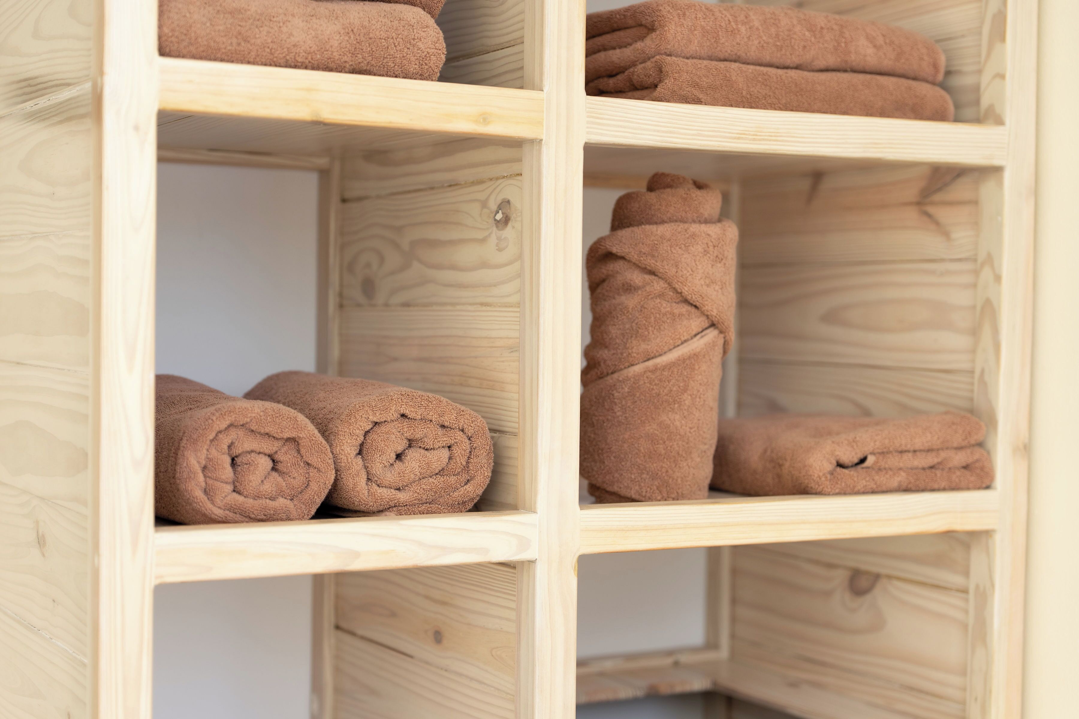 A wooden shelf unit with neatly rolled brown towels.