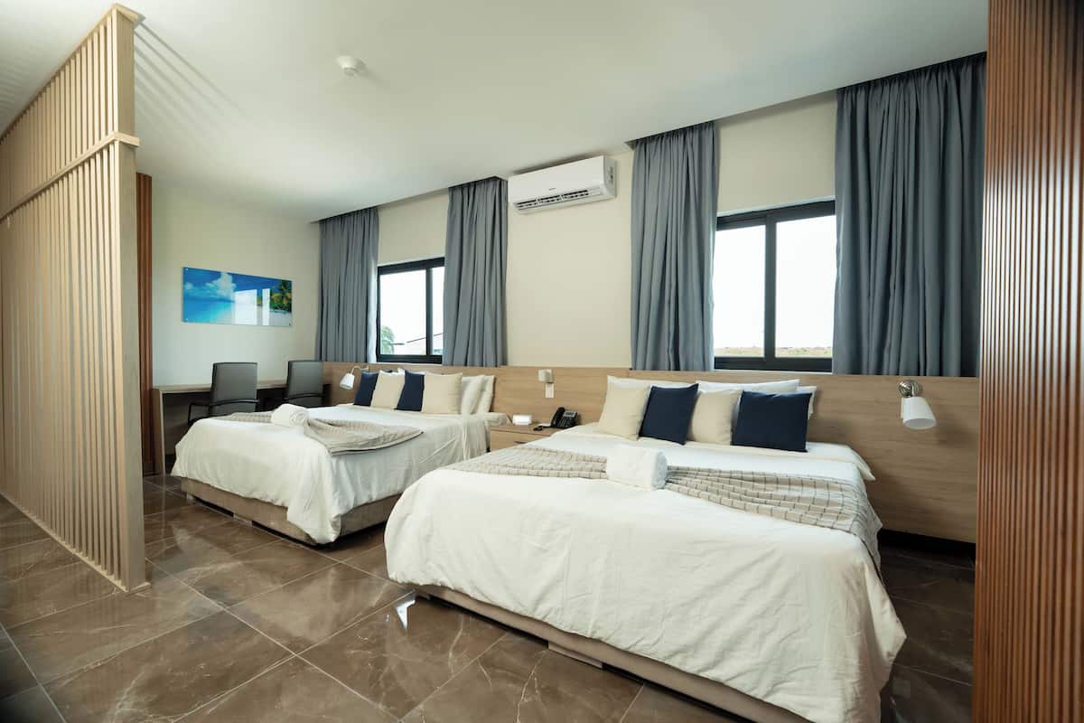 A hotel room with two beds, a desk, a chair, an air conditioning unit, and a painting on the wall.