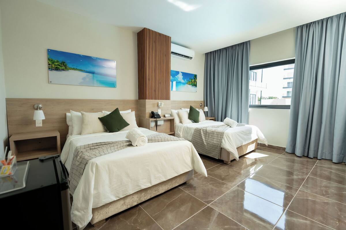 A hotel room with two beds, a nightstand, a desk, and a window with curtains.