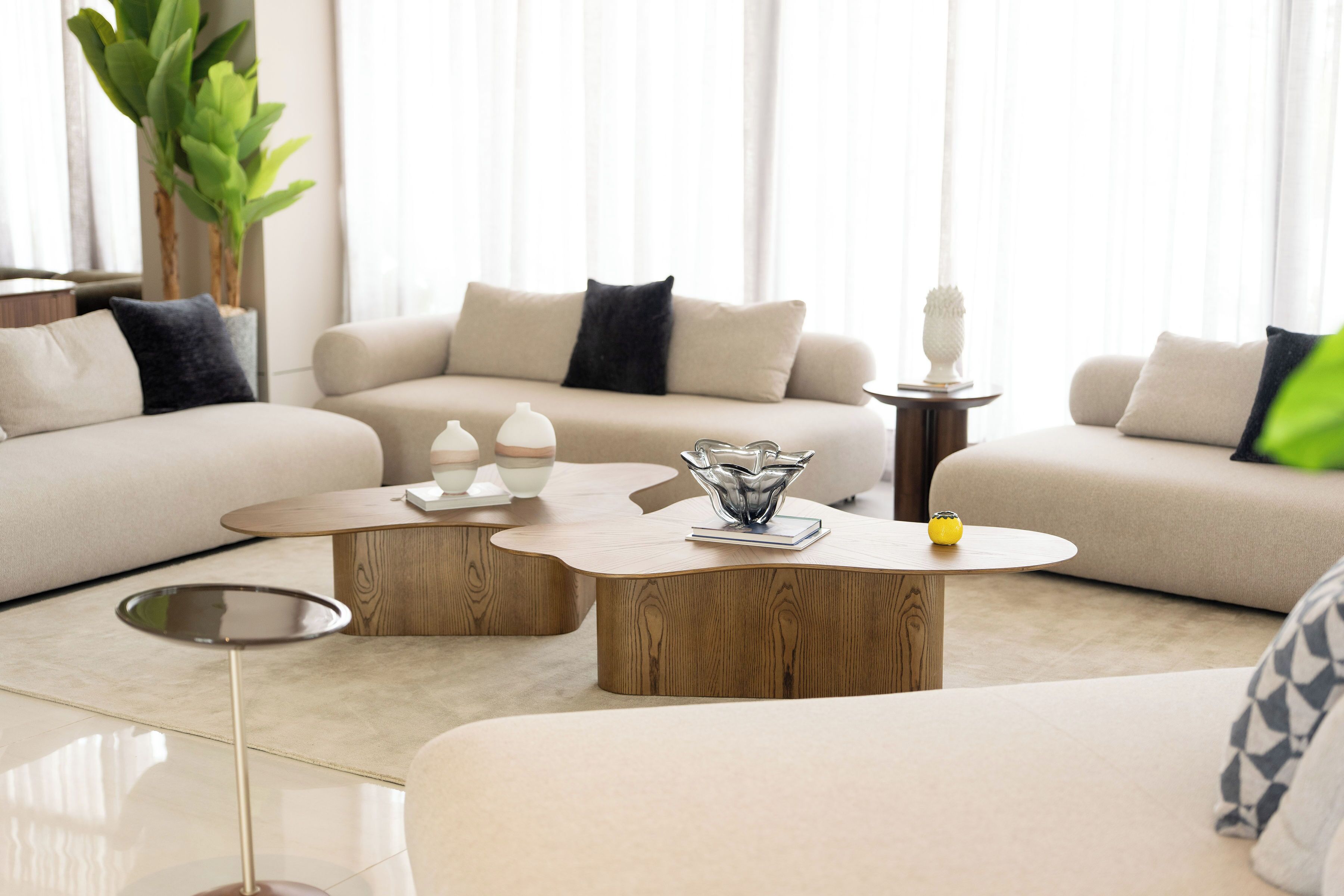 A modern living room with a beige sofa, two wooden coffee tables, and a glass vase.