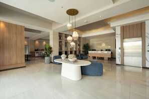 Una hall moderna di un hotel con un'area salotto centrale, una reception e un ascensore ben visibile.
