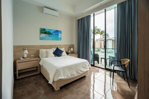 Camera d'albergo con un letto grande, un comodino con una lampada, una sedia e vista sull'esterno tramite una porta scorrevole in vetro.