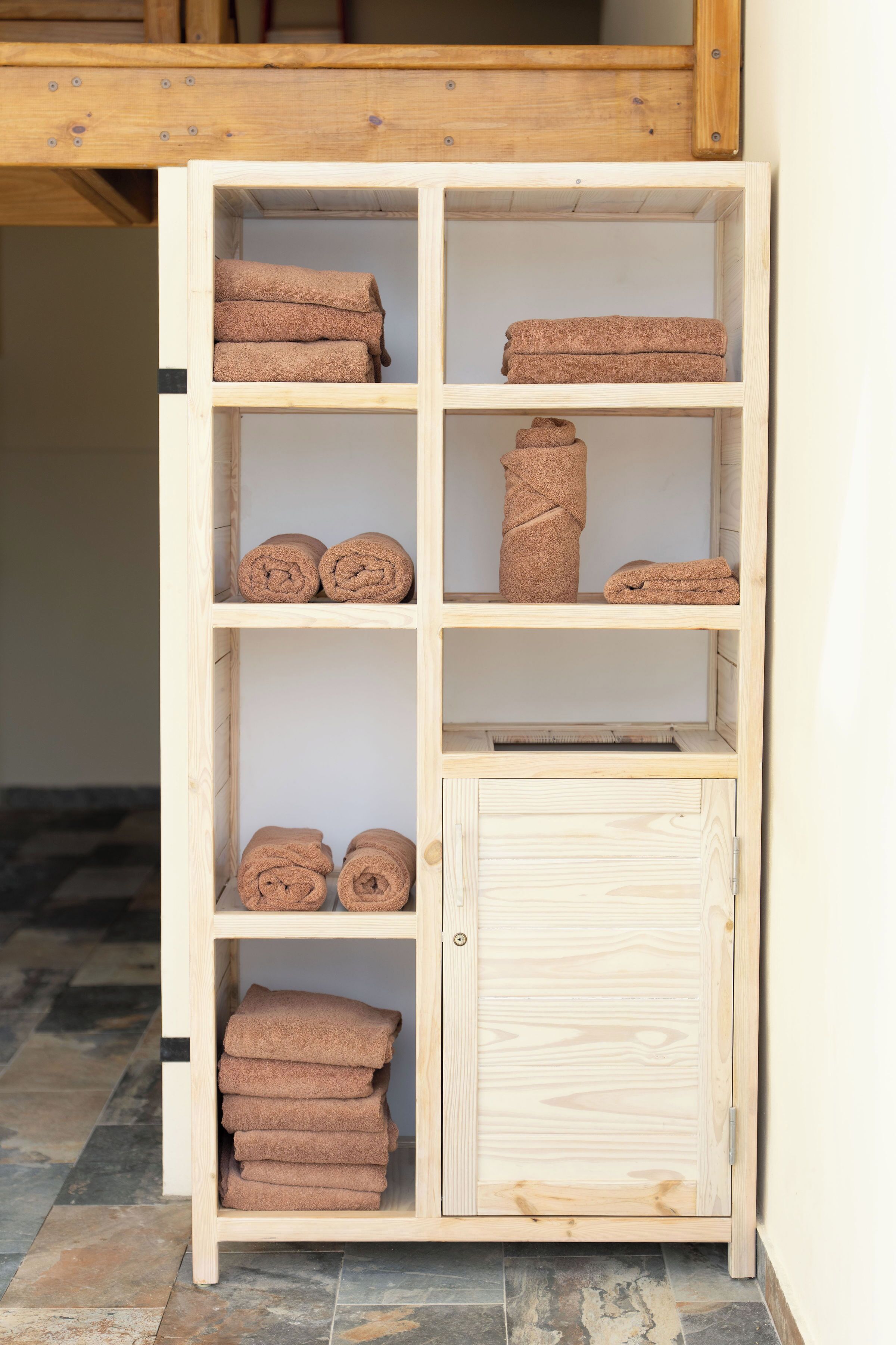 A wooden shelf unit with multiple compartments, some containing folded towels.