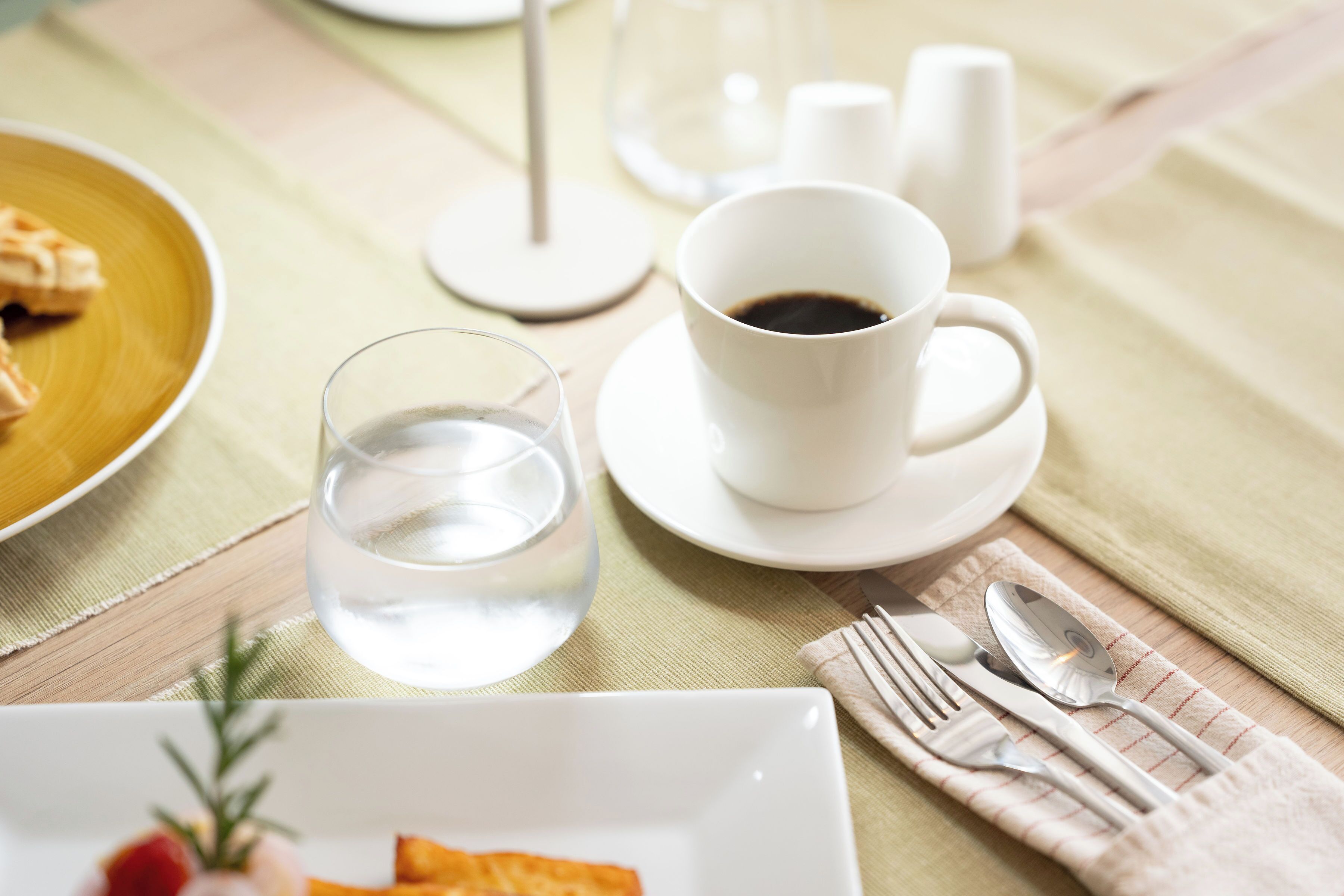A table with a white cup of coffee, a glass of water, and a plate of food.