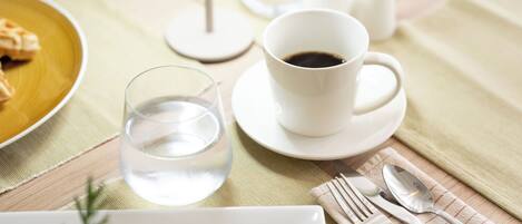 A table with a white cup of coffee, a glass of water, and a plate of food.