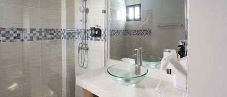 A modern bathroom with a glass shower enclosure, a glass sink, and a large mirror.
