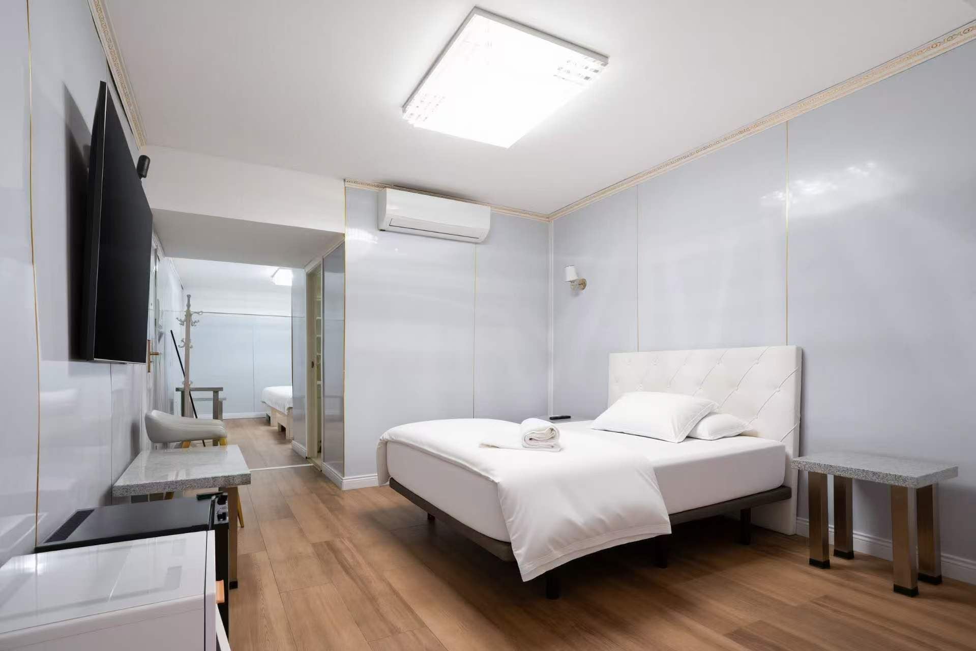A hotel room with a bed, a bedside table, a TV mounted on the wall, and a ceiling light.