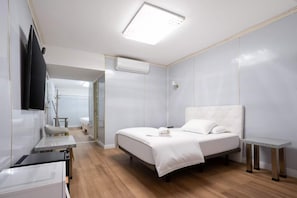 Une chambre d’hôtel avec un lit, une table de chevet, un téléviseur fixé au mur et un luminaire au plafond.