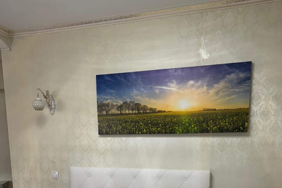 Una cama bien hecha con cabecera, dos mesitas de noche y una lámpara de pared.
