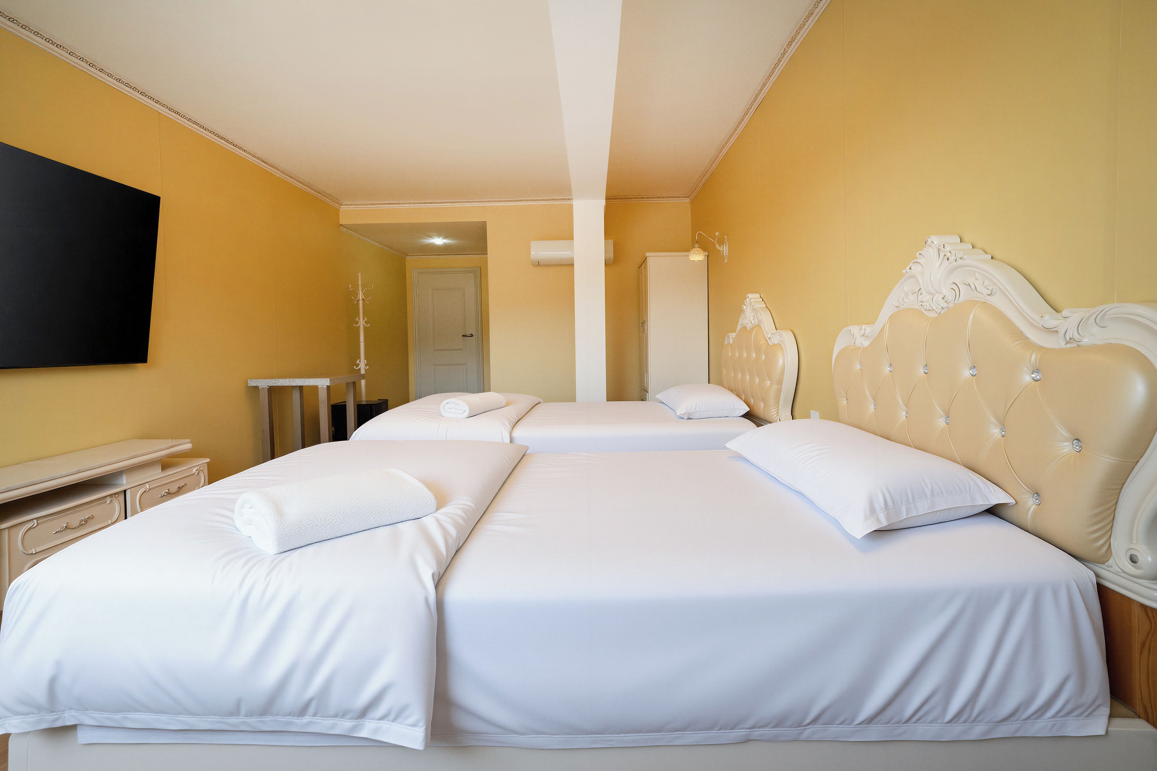 Habitación de hotel con dos camas, un televisor de pantalla plana en la pared y un perchero.