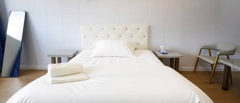 A neatly made bed with pillows, a bedside table with a lamp, a chair, and a large mirror on the wall.