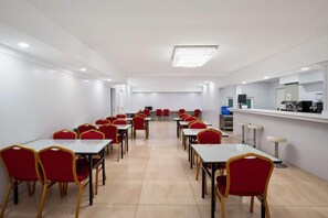 A conference room with rows of tables and chairs, a kitchenette, and a door leading to another room. - air hotel aviacion  (Manises)