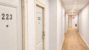 Un pasillo con puertas numeradas 223 y 222, piso de madera y luces empotradas en el techo.